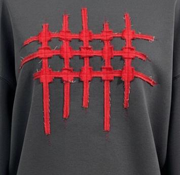 Close-up van de handgemaakte raster-applicatie van rauw, rood denim op de antracietkleurige sweater.